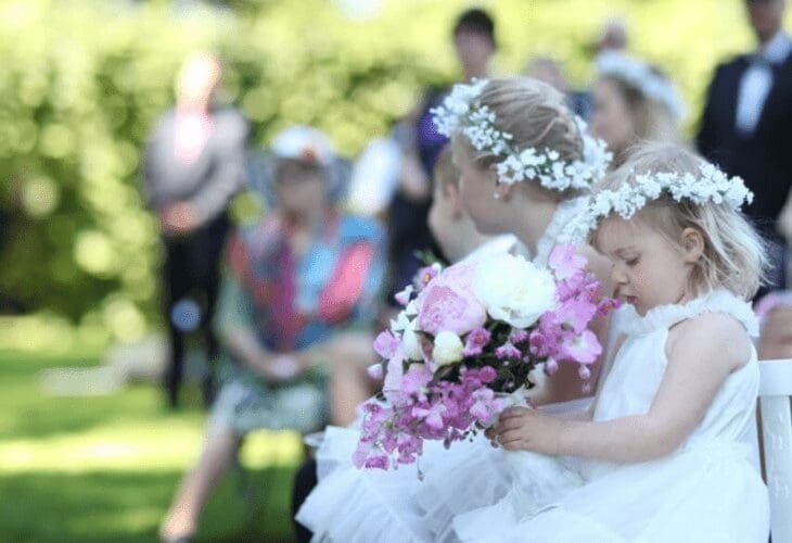 To små jenter ikled hvite kjoler og hvit blomsterkrans, holder en rosa brudebukett