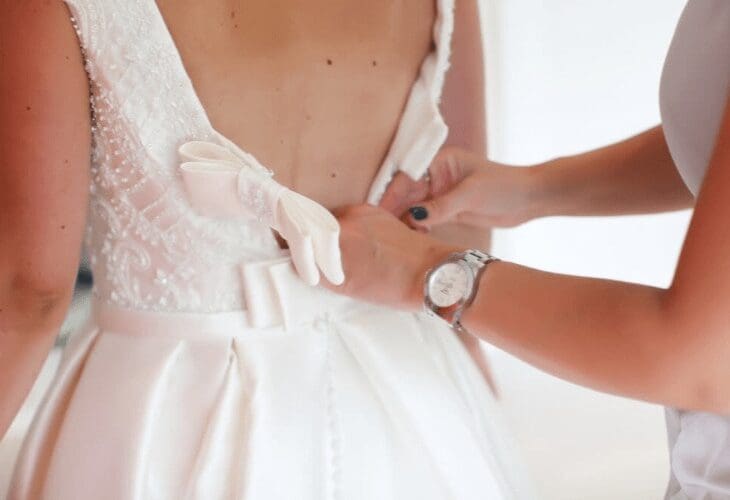 Kvinne knepper igjen ryggen på en brudekjole på en brud