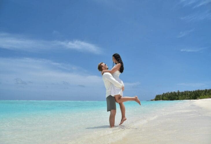 Mann løfter en kvinne på en strand i syden på en solfylt dag