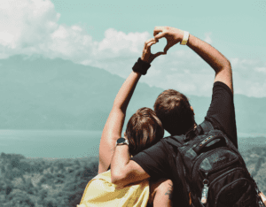 Par lager hjerte med hendene på fjelltopp med utsikt i bakgrunnen