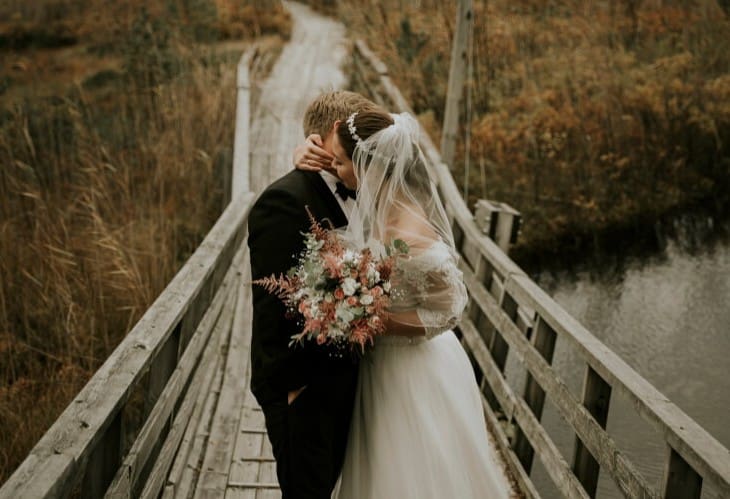 Brudepar omfavner hverandre på en trebru på høsten