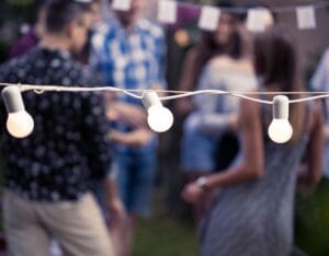 Uklar bakgrunn med mennesker som danser, og en lyslenke på tvers i fokus. Hageleker til bryllupet, kan bestå av dans og husk lyslenker til mørket og kvelden.