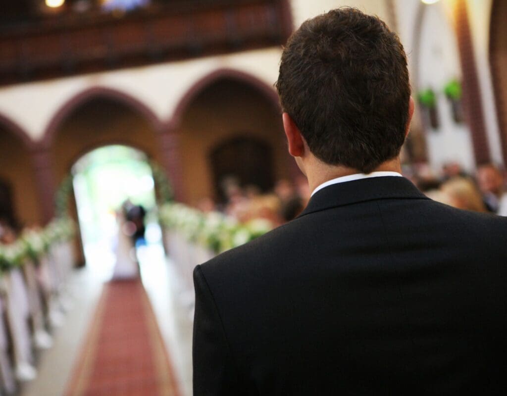 Brudgom står med ryggen til og venter på bruden i kirken