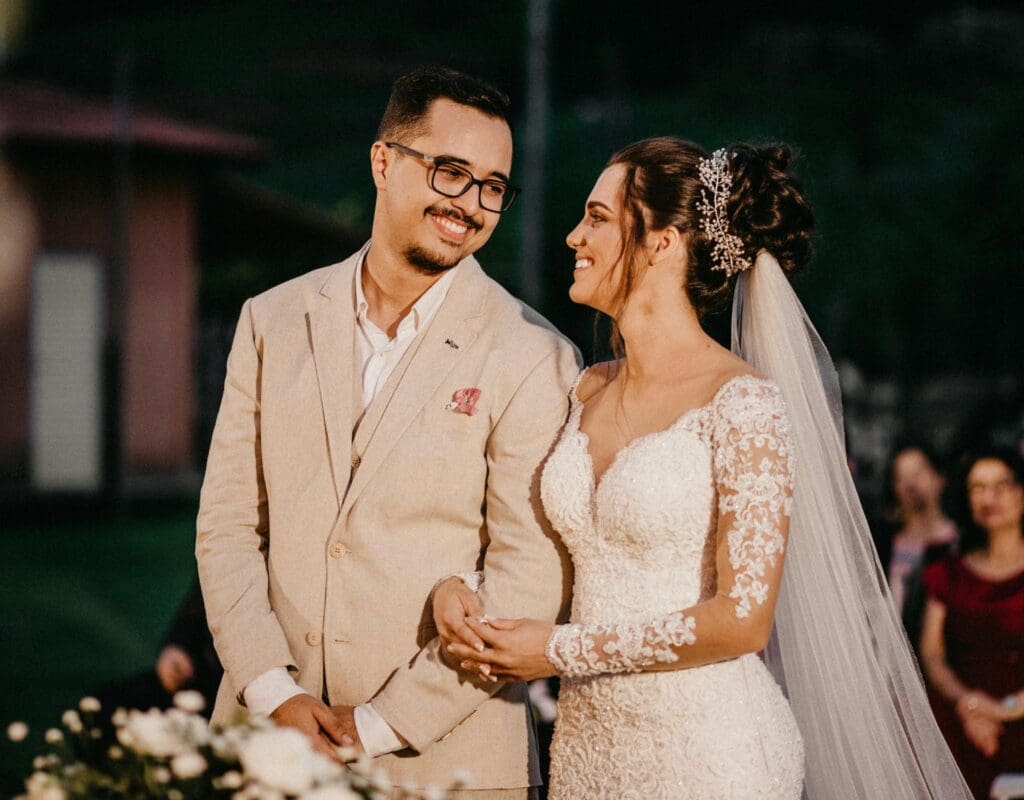 et par står sammen under vielsen i kirken, de holder hender, ser på hverandre og smiler, i bakgrunnen ser vi noen av gjestende sittende