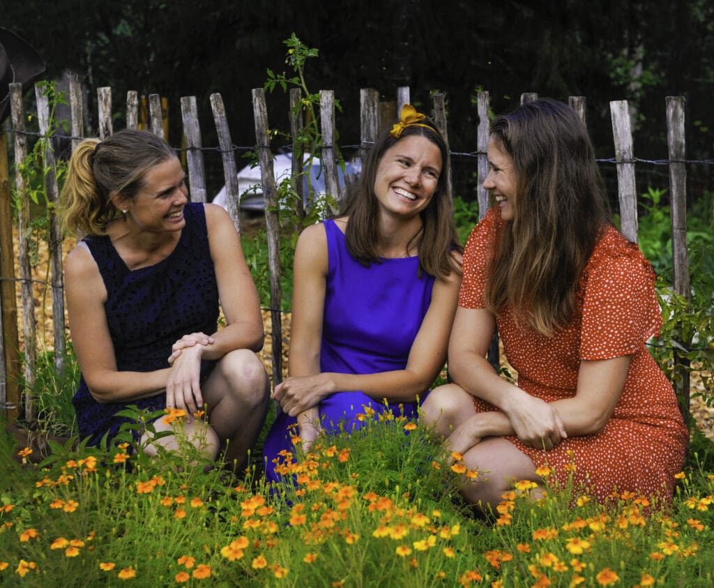 Søstrene Storaas Solveig, Else og Henriette sittende blant oransje blomster og smiler til hverandre