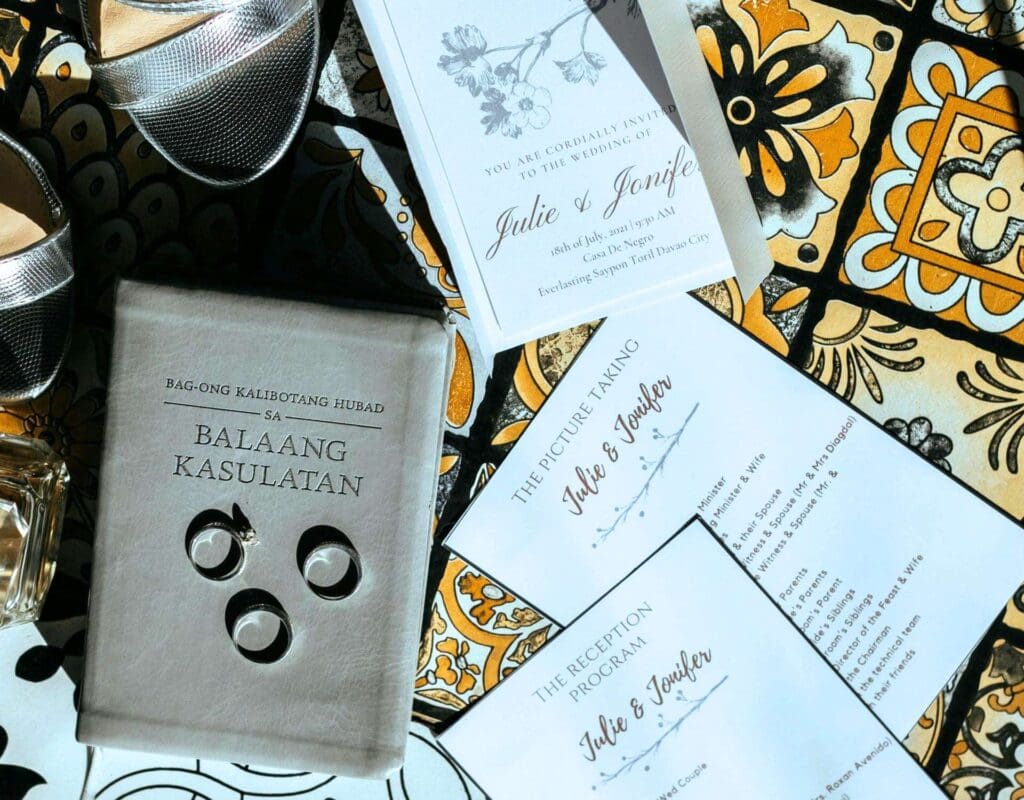 Bryllupsinvitasjoner på et bord sammen med bryllupssko, gifteringer og forlovelsesringer.