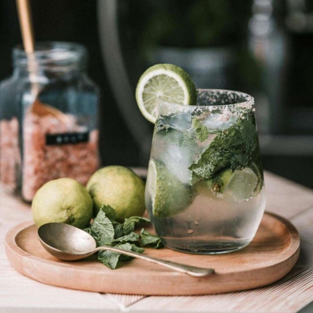 Mojito drink på et trefat med lime og sukkerglass i bakgrunnen