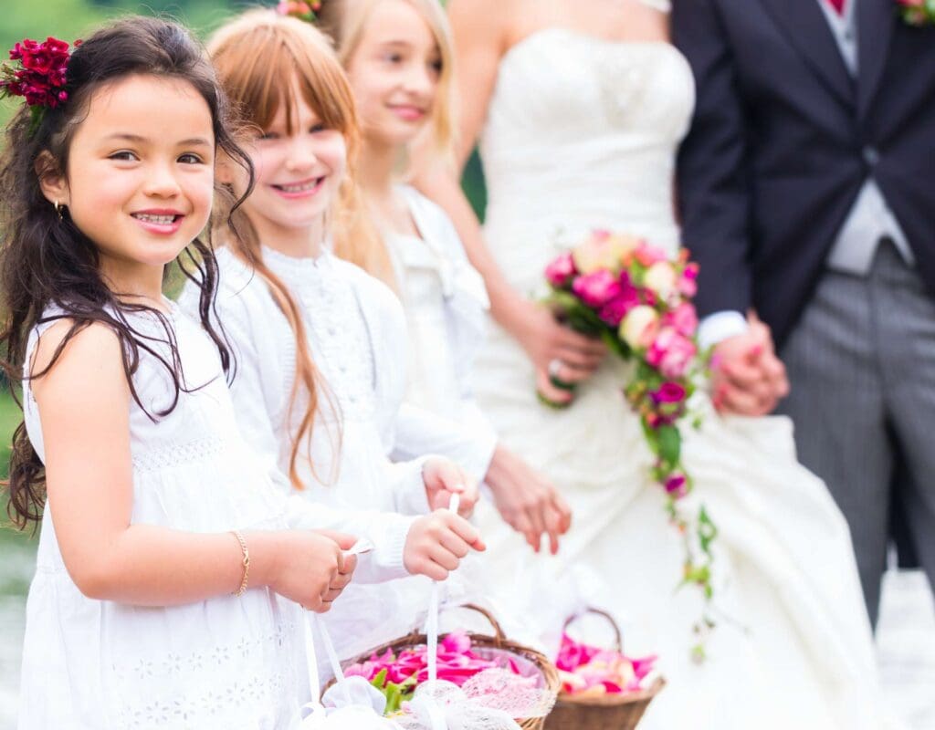Tre jenter i bryllup som holder blomsterkurver, med brudeparet i bakgrunnen. Representerer blomsterpiker i en vielse. Skal vi ha barn i bryllupet? under vielsen er det veldig søtt.