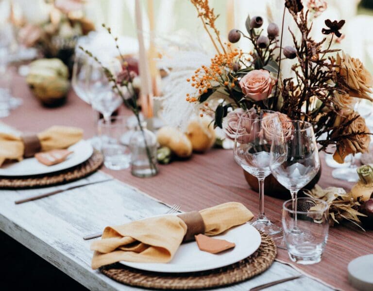 Bryllupsbord med elegant oppsett av tallerkener og bestikk, prydet med en stor blomsterdekorasjon.