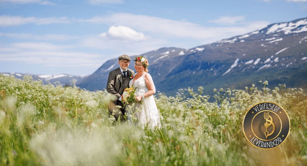 Et brudepar poserer sammen i en blomstereng med fjell i bakgrunn på Bortistu Gjestegaard