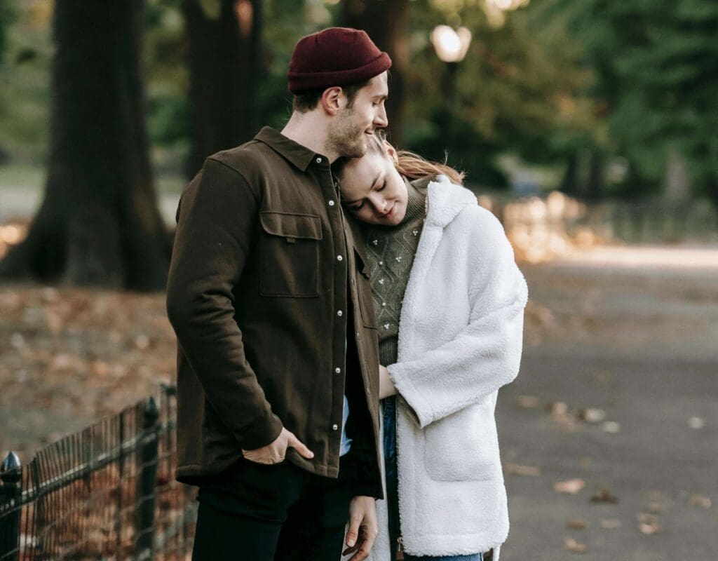 Et par i casual klær, kvinnen hviler hodet på mannens skulder, ute i friske høstfarger og høstluft. Representerer det å ta vare på hverandre selv om man må utsette et bryllup.