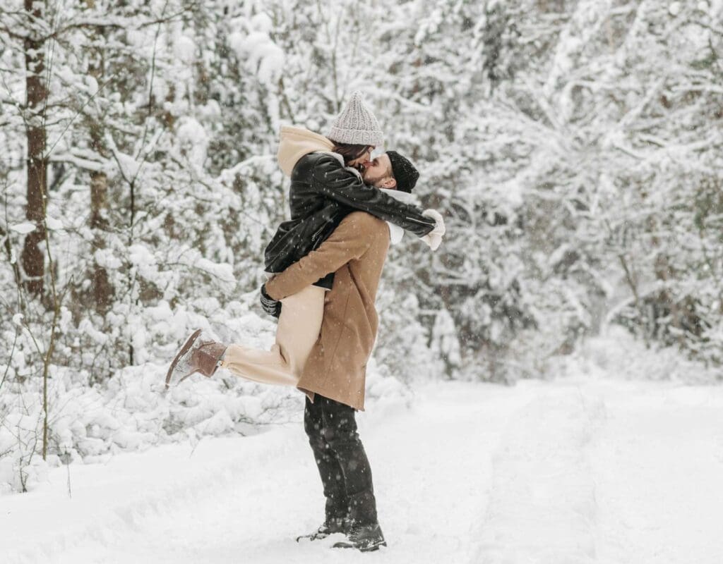 Par i snøen i skogen som feirer kjærligheten; hun hopper opp og blir holdt av ham mens de kysser. Det er masse snø rundt dem, og skikkelig vinterlandskap.