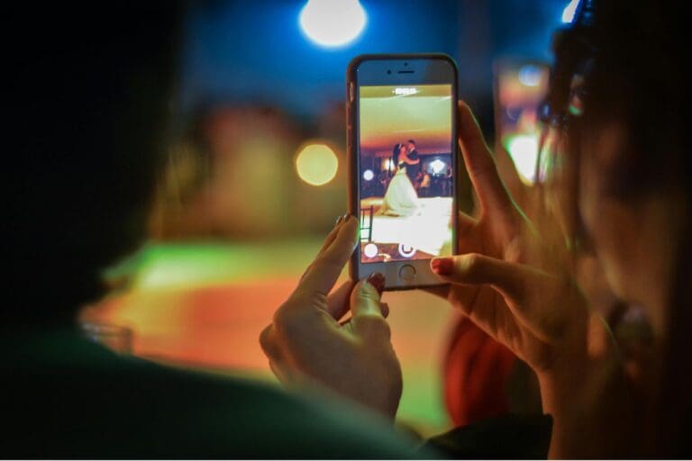 En kvinne ser på et brudepar som danser på en mobiltelefon, som representerer et digitalt bryllup