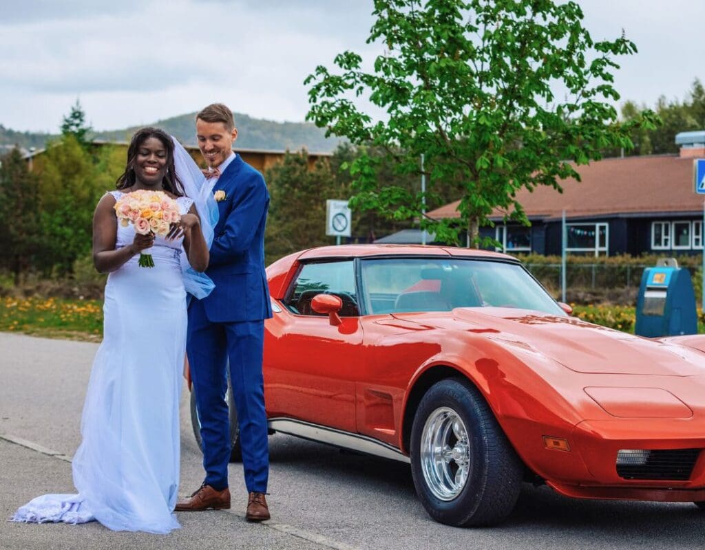 Et gift par står foran en rød Corvette bryllupsbil
